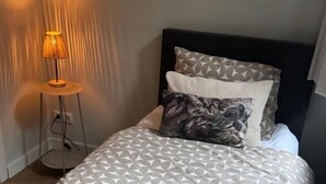 Una cama bien hecha con ropa de cama estampada, una lámpara de noche y un cabecero oscuro.