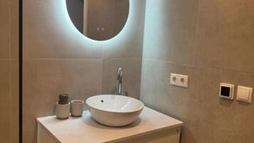 Un baño con un espejo redondo, un lavamanos sobre encimera y un armario.