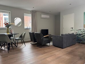 Een moderne woonkamer met een bank, stoelen, een televisie en een eettafel.