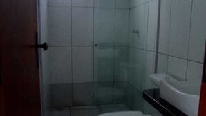 Un pequeño espacio de ducha cerrado con puerta de vidrio, un inodoro blanco y una encimera negra.
