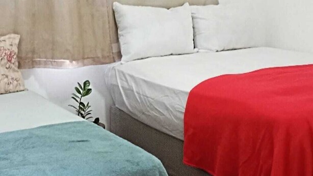 Habitación de hotel con dos camas, una con una manta roja y la otra con una manta azul.