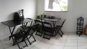 Un pequeño comedor con una mesa, cuatro sillas, una máquina de café, una ventana con vistas al exterior y una planta sobre la mesa.