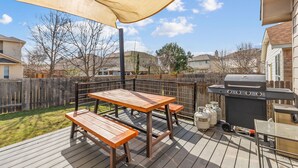 Une terrasse à l’arrière de la maison, équipée d’un barbecue, de tables en bois et d’un auvent.