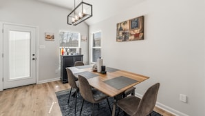 Un coin repas comprenant une table en bois, quatre chaises, un tapis, une suspension et un tableau accroché au mur.