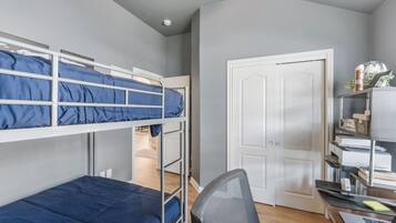 A bunk bed room with a desk and chair, a white door, and a shelf with books and a lamp.