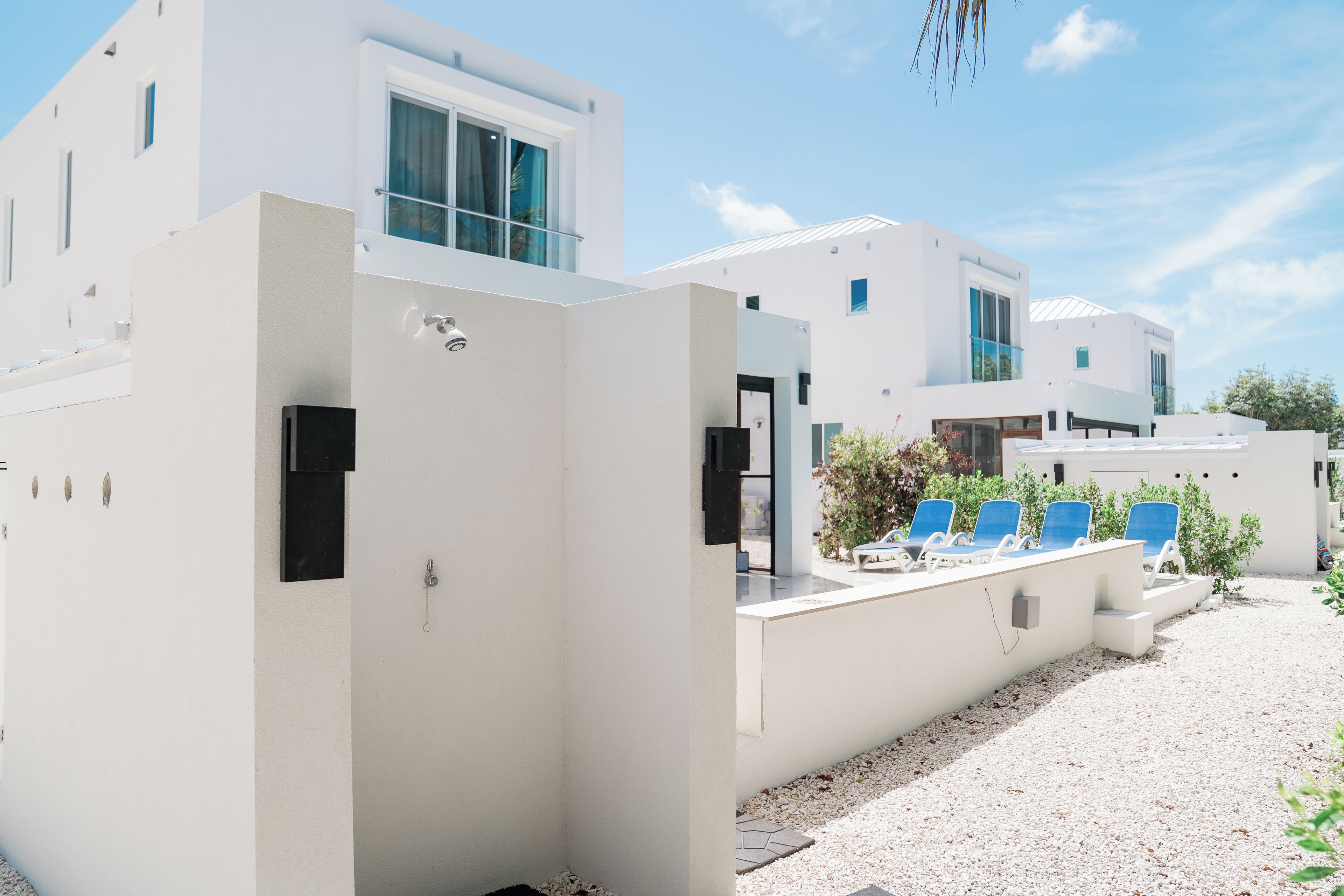 Un bâtiment moderne à l’extérieur blanc, doté de grandes fenêtres et d’un espace extérieur aménagé avec des chaises bleues.