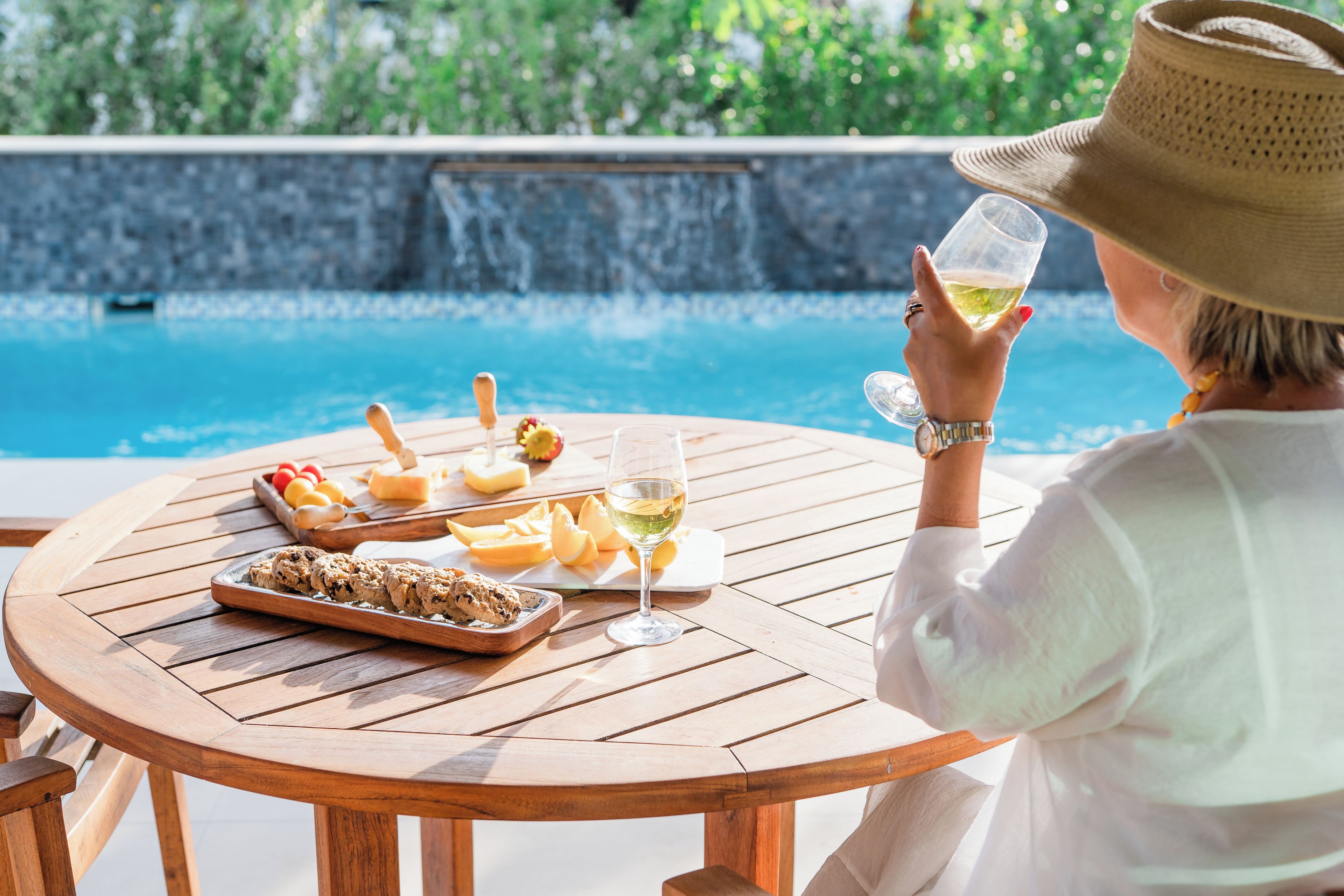 A round wooden table with a glass of white wine, a plate of cookies, and a fruit platter.