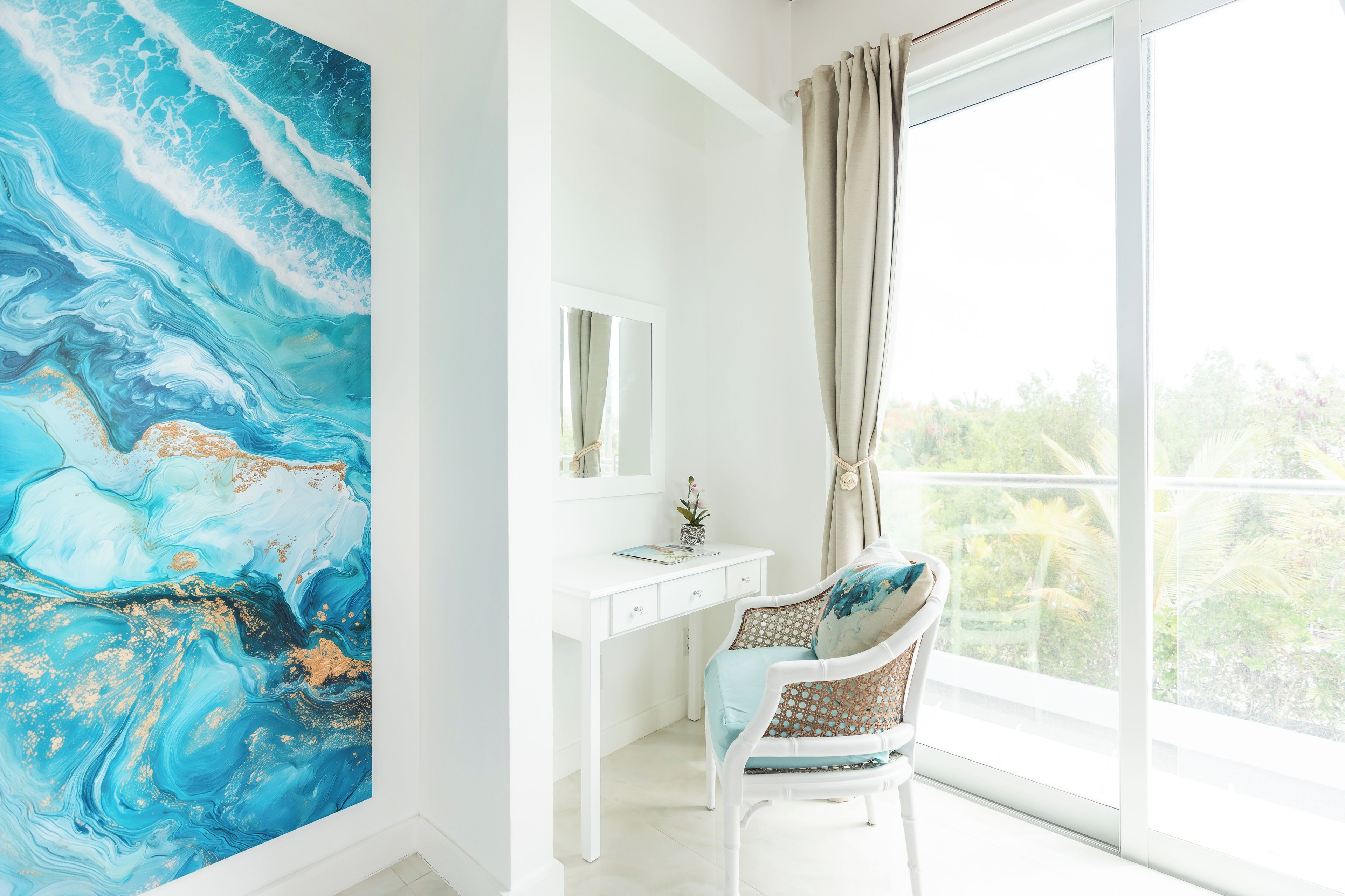 A room with a large abstract painting, a white desk, a chair, and a large window with a view of greenery.