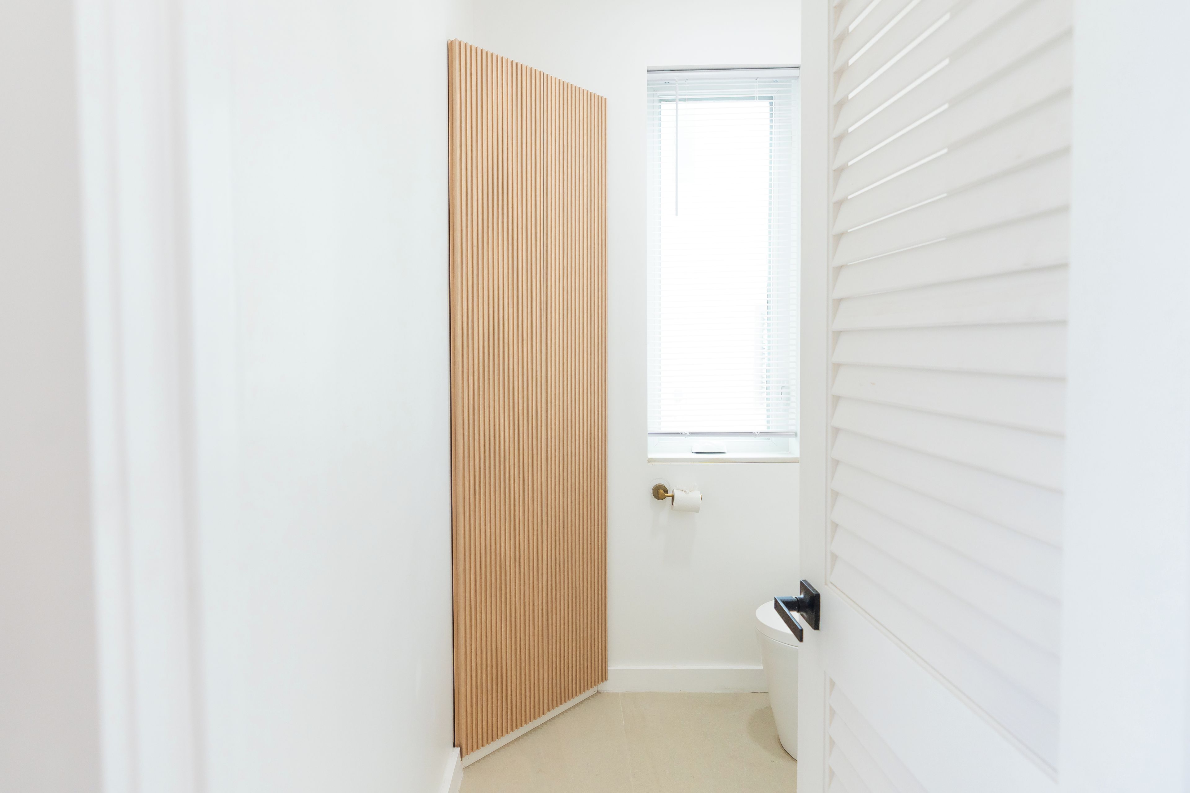 A narrow hallway with a wooden door, a window with blinds, and a white radiator.