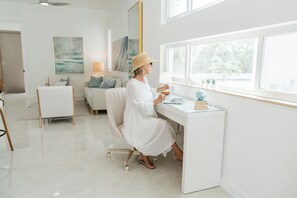 Habitación moderna y luminosa con un escritorio blanco, una silla cómoda y un amplio ventanal con vistas a zonas verdes.