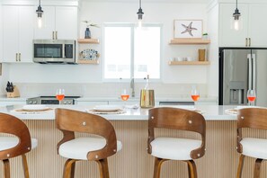 A modern kitchen with white cabinets, stainless steel appliances, and wooden chairs with white cushions. - Luxury New Grace Bay Villa/ private pool/2 min walk to reef, beach, restaurants (The Bight Settlement)