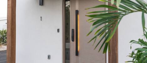 En modern entré med en träpergola, en skjutglasdörr och en liten uteplats med ett betonggolv.