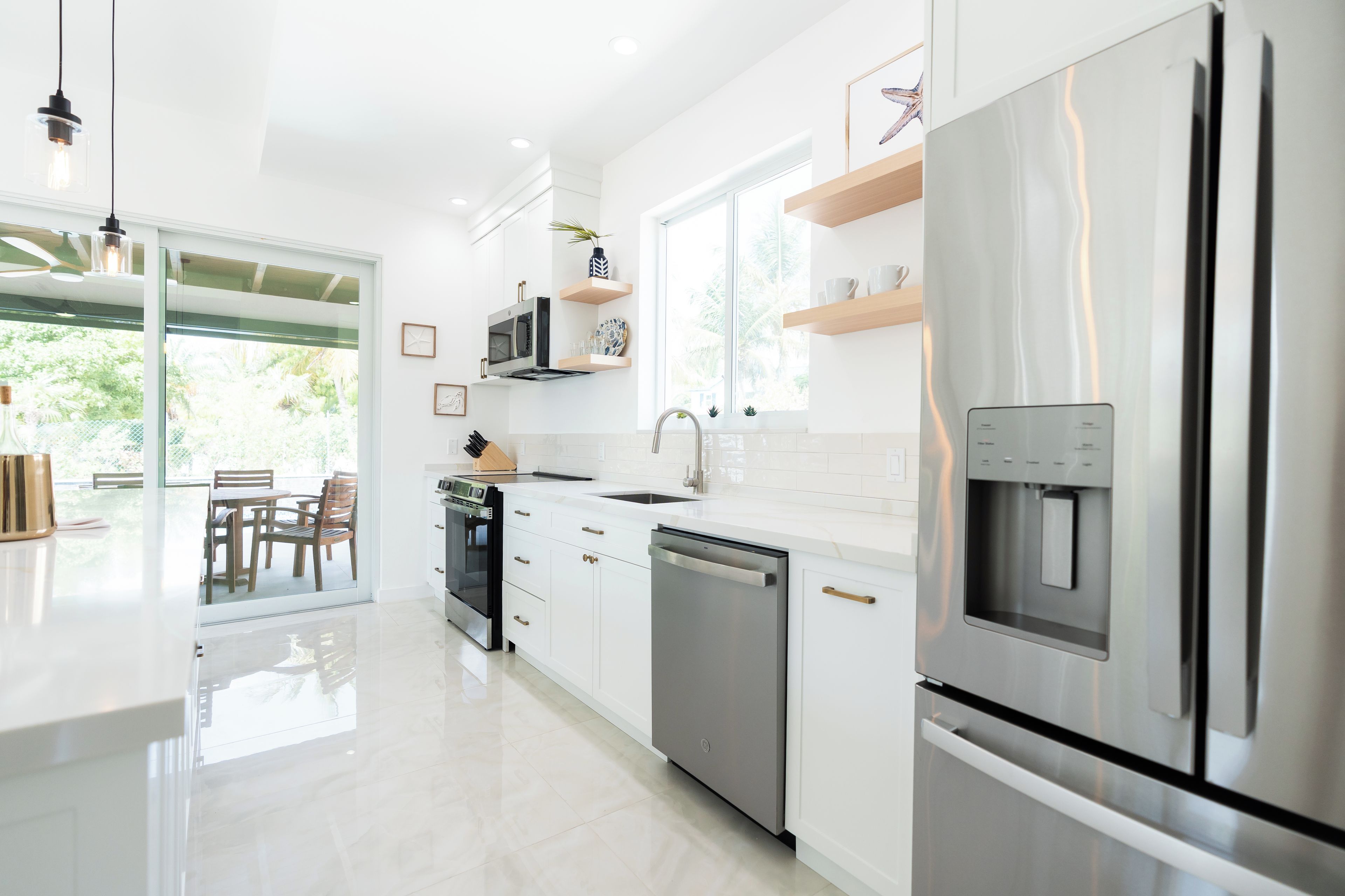 A modern kitchen with stainless steel appliances, white cabinetry, and a large window providing natural light.