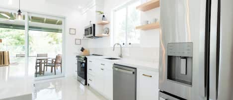 Una cocina moderna con electrodomésticos de acero inoxidable, armarios blancos y un amplio ventanal que proporciona luz natural.