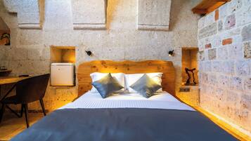 A bedroom with a wooden headboard, a bed with pillows, a desk, and a small refrigerator.
