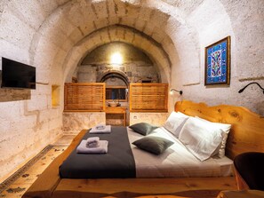 Una habitación con paredes de piedra, una cama, persianas de madera, un lavamanos y un televisor.