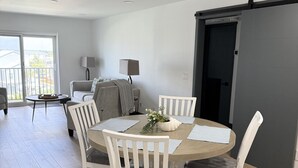 Ein modernes Wohnzimmer mit Esstisch, weißen Stühlen, einer Couch und einer Schiebetür.
