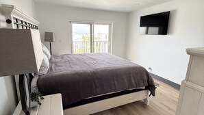 Ein Schlafzimmer mit Bett, Fernseher, Fenster und Balkon.