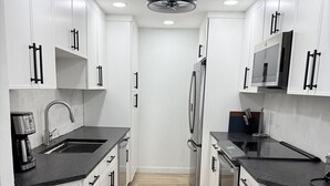 Eine moderne Küche mit weißen Schränken, schwarzen Griffen, einem Edelstahl-Kühlschrank, einer Mikrowelle und einer Kaffeemaschine.