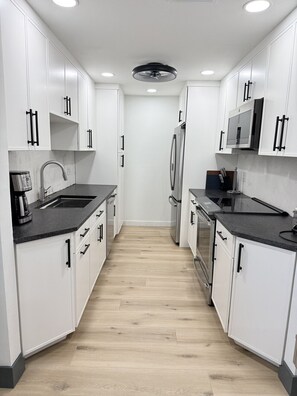 Eine moderne Küche mit weißen Schränken, schwarzen Griffen, einem Edelstahl-Kühlschrank, einer Mikrowelle und einer Kaffeemaschine.