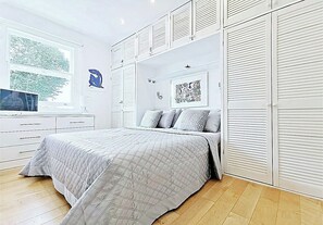Ein Schlafzimmer mit Bett, Fernseher, Fenster und Kleiderschrank.