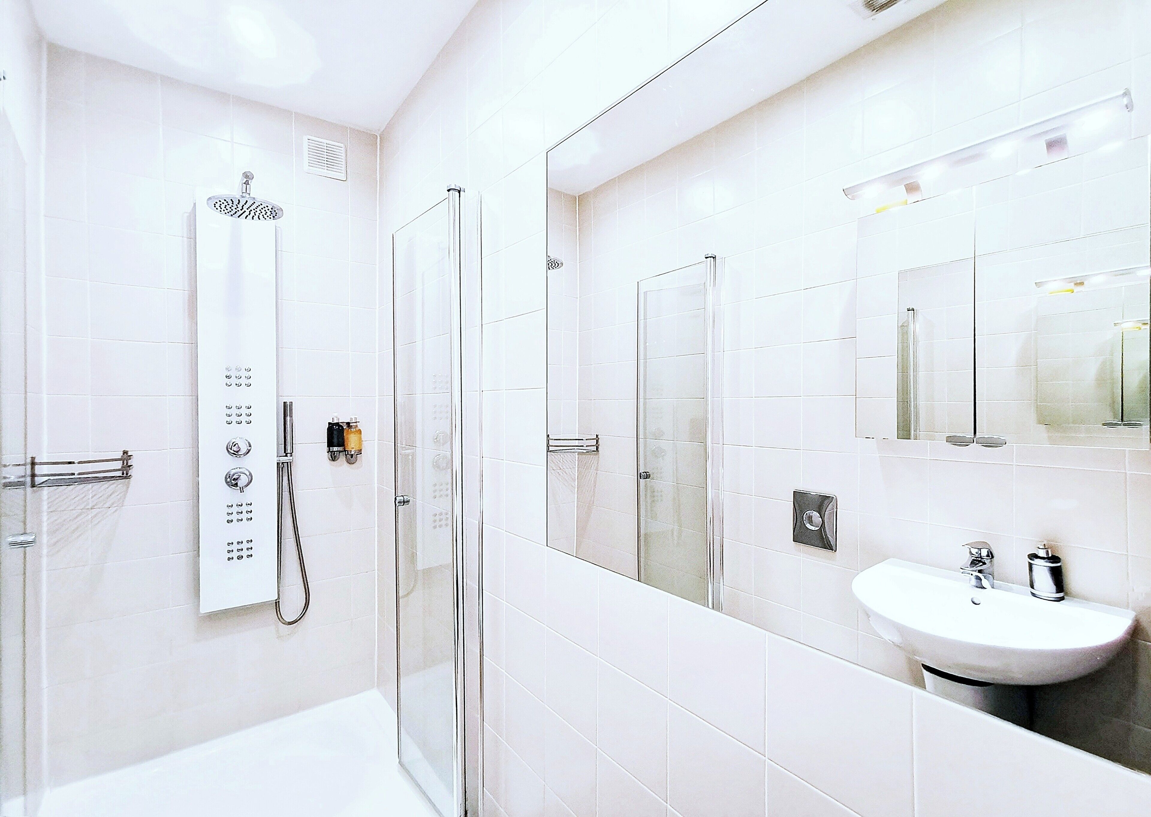 A modern bathroom with a glass-enclosed shower, a white sink, and a large mirror.