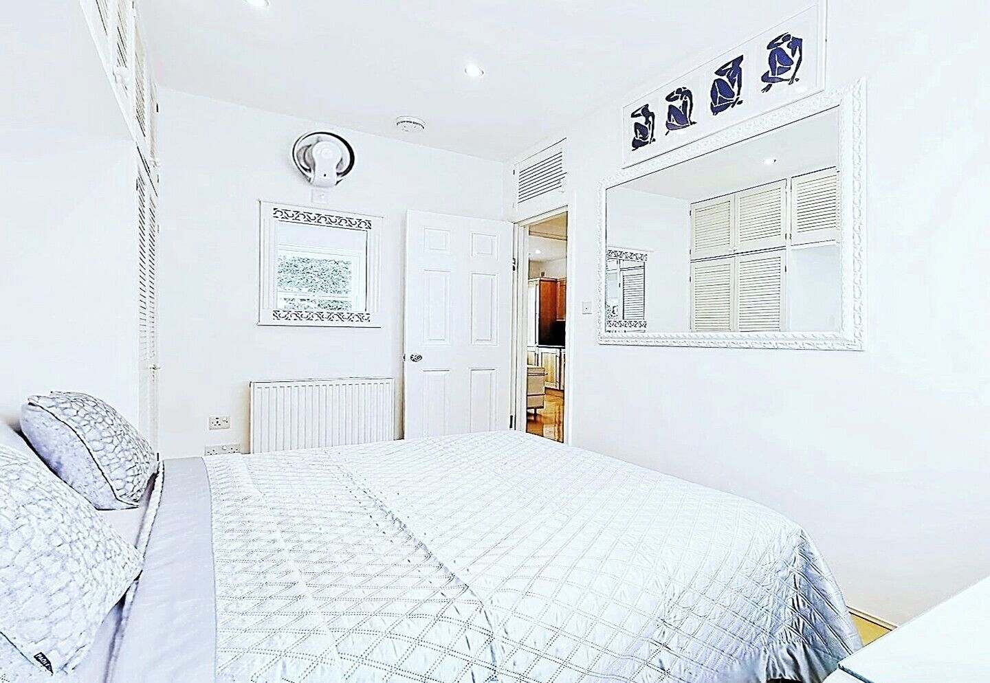 A bedroom with a bed, a radiator, a door, and a wall with framed pictures.
