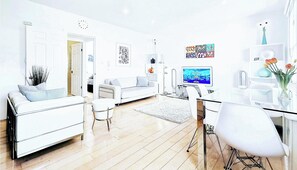 Ein modernes Wohnzimmer mit einem weißen Sofa, einem Glastisch und einem Flachbildfernseher.