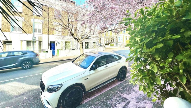 En hvid bil parkeret på en gade med bygninger i baggrunden.