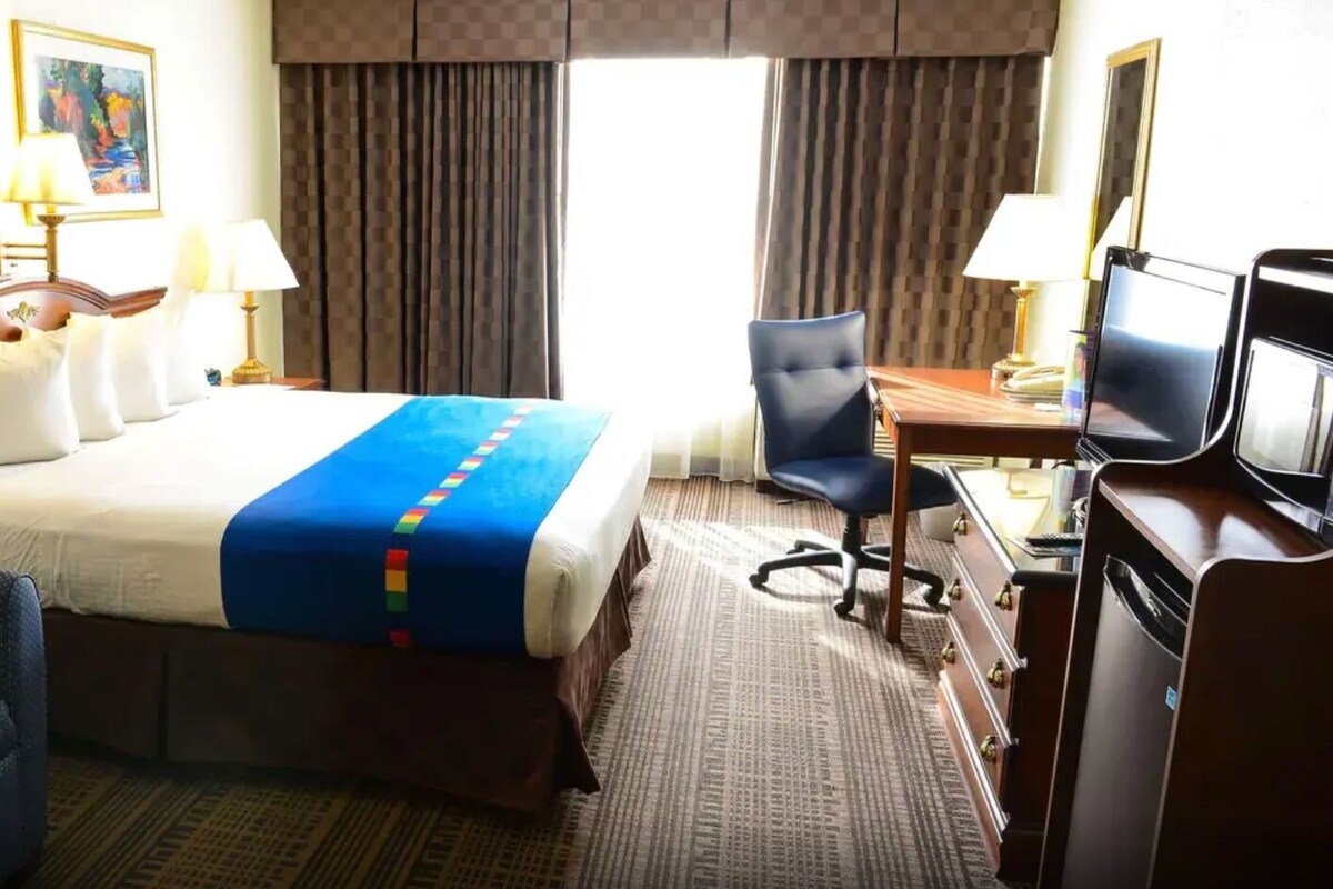 A hotel room with a bed, a desk with a chair, a television, and artwork on the walls.