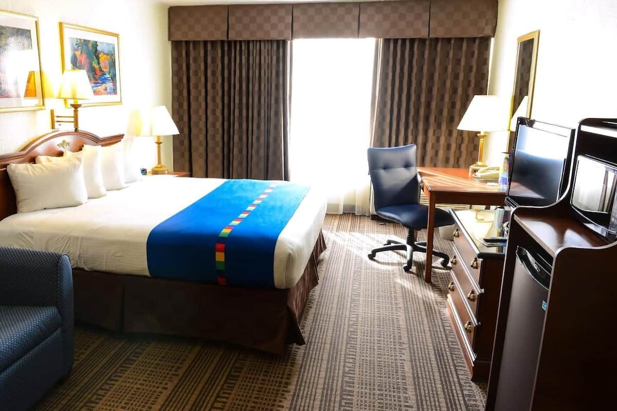 A hotel room with a bed, a desk with a computer, a chair, and a television.