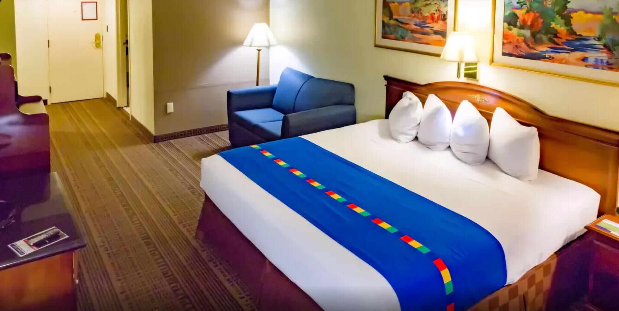A hotel room with a bed, a chair, a desk, and a lamp.