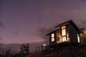 Ein modernes Haus mit großem Fenster und Balkon, umgeben von Bäumen und einem bewölkten Himmel.