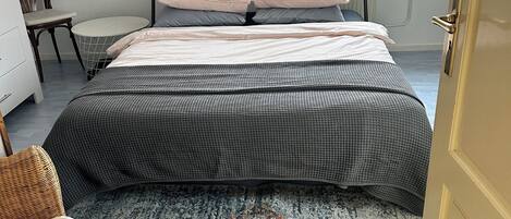 Un dormitorio con cama, una silla, una mesita y una ventana.