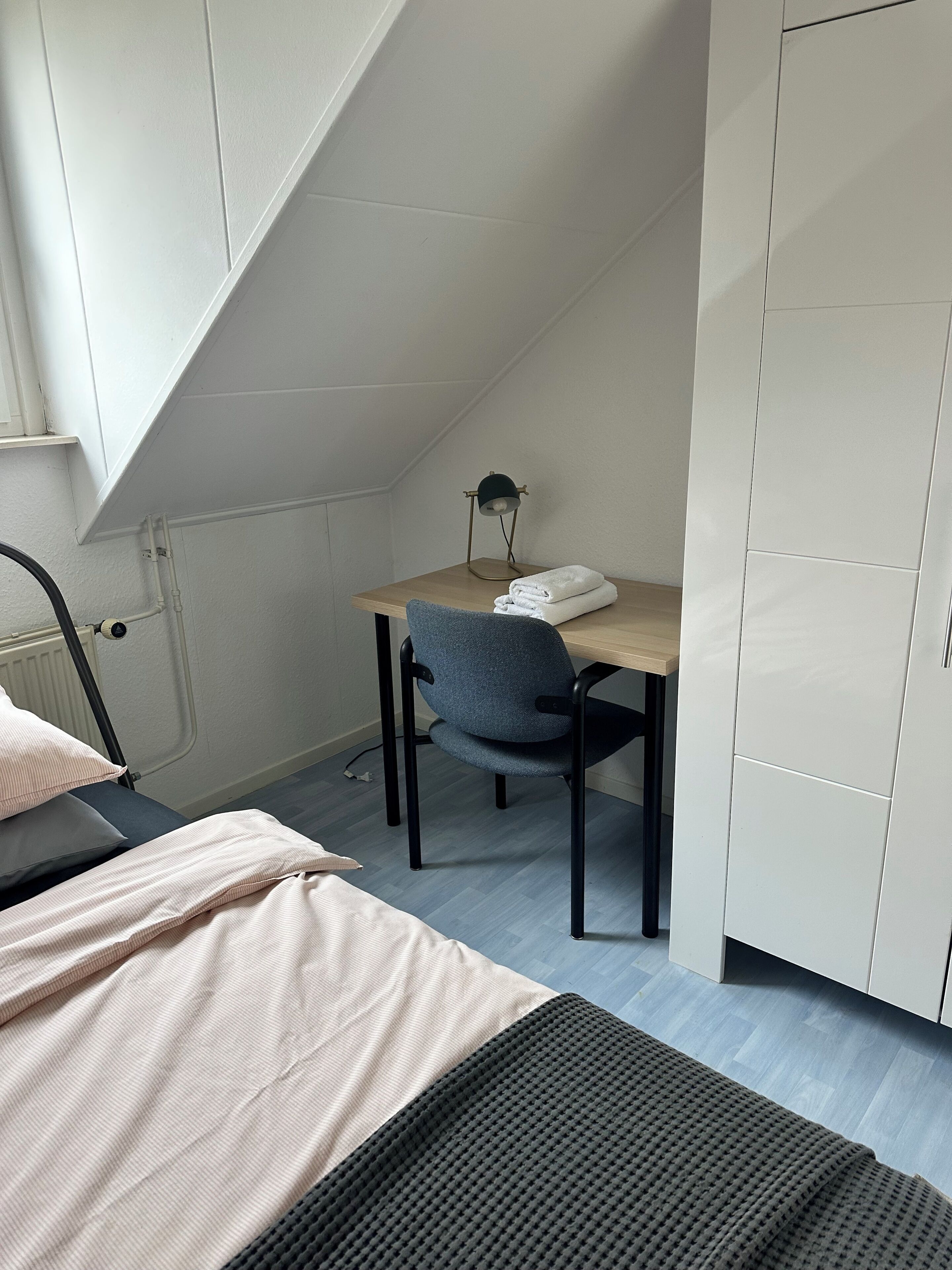 Et soveværelse med en seng, et skrivebord med stol, en radiator og et garderobeskab.