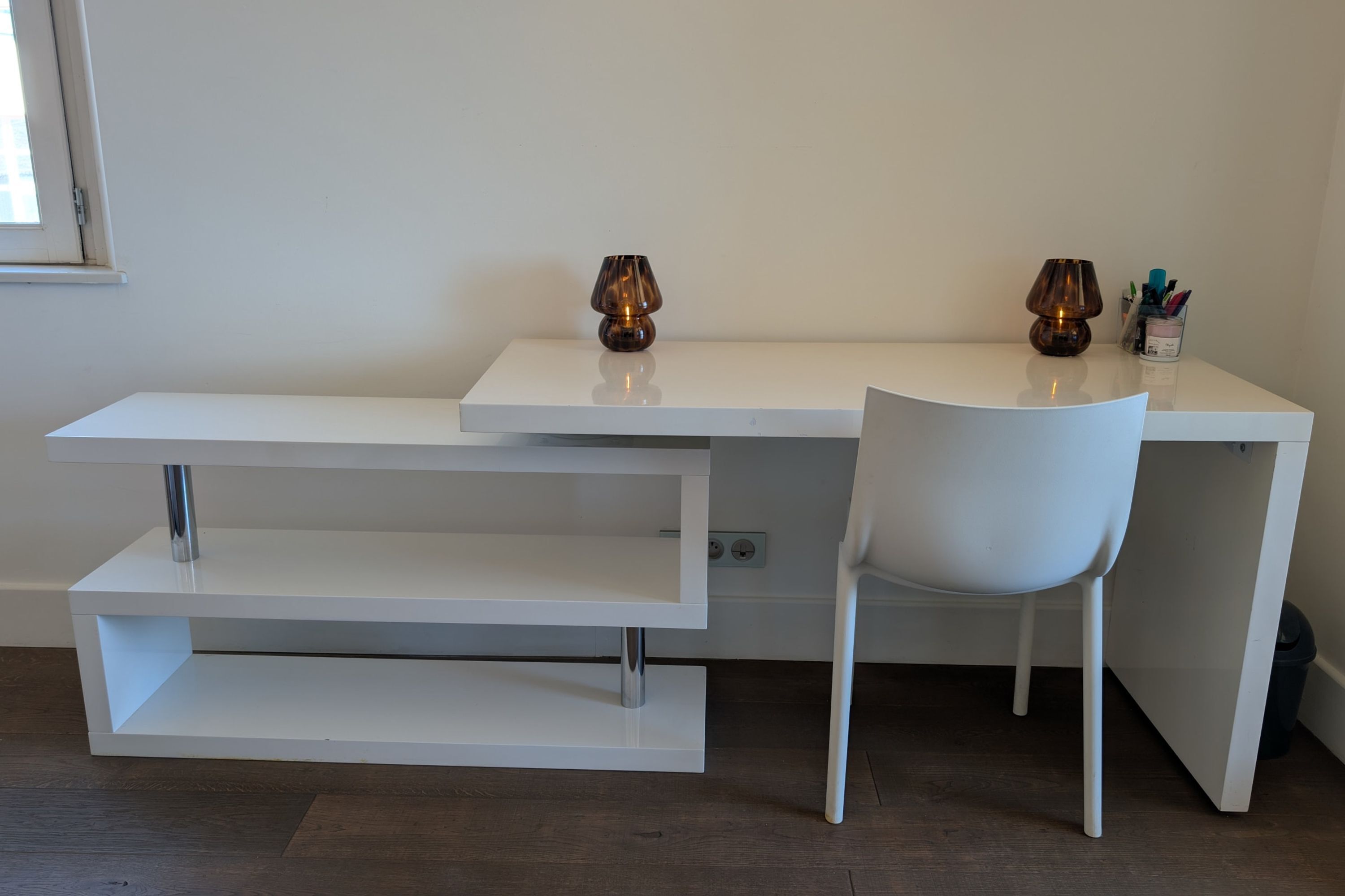 Een wit bureau met een stoel, twee lampen en een pennenhouder.
