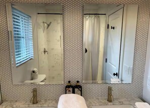 A bathroom with two sinks, a shower, a toilet, and a large mirror.