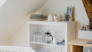 Una cocina con armarios blancos, un banco de madera y una cafetera en el estante.