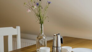 Una mesa de comedor con un florero, una cafetera y tazas blancas.
