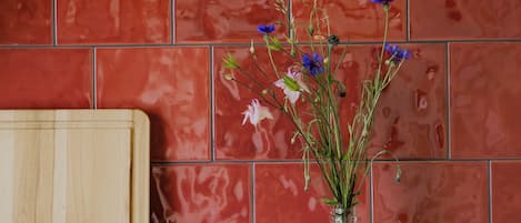 Una encimera de cocina con una cafetera, un florero de vidrio con flores y una tabla de cortar de madera.