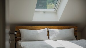 Un dormitorio con cabecera de madera, dos almohadas blancas y un tragaluz sobre la cama.