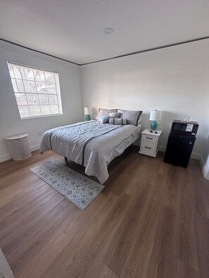 A bedroom with a bed, bedside tables, a lamp, a microwave, and a window with blinds. - Hotel Style 1-bedroom in lovely Orlando with AC (Orlando)