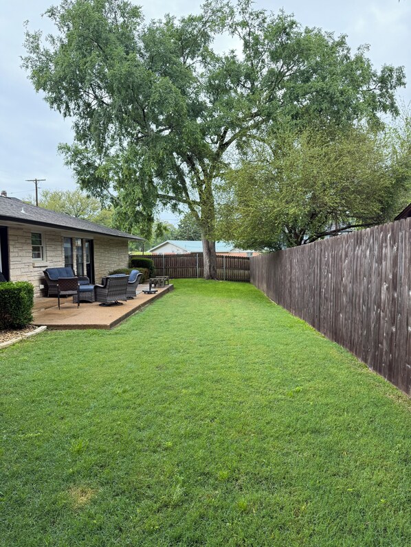 A backyard with a stone house, a wooden fence, and a tree.
