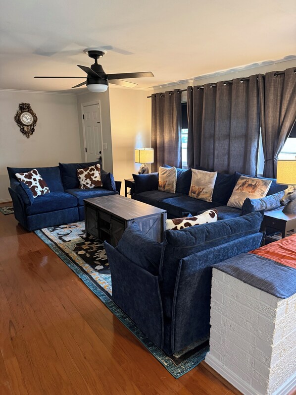 A living room with a blue sofa set, a wooden coffee table, a ceiling fan, a lamp, and a patterned rug.