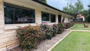 A building with a stone facade, large windows, and a well-maintained lawn with flowering bushes.