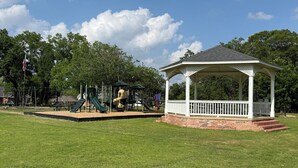 A gazebo with a brick base and white railings, a playground with slides and swings, and a flagpole with an American flag.