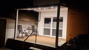 A covered patio with a table and chairs, a brick wall, and a window with blinds. - Vacation apartment Lichtblick in a quiet location / free parking and WLAN (Sulingen)