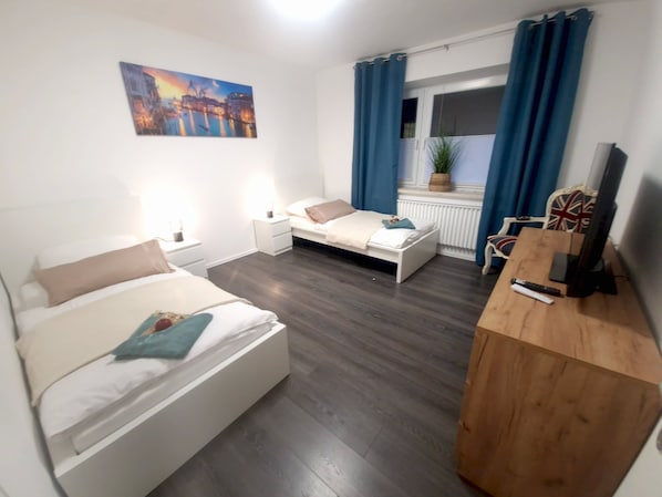 Un dormitorio con dos camas, un escritorio de madera, un televisor y una ventana con cortinas.