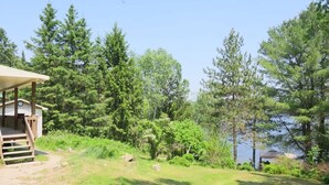 Mökki, jossa on terassi, ja sen ympärillä on tiheää metsää ja järvi.