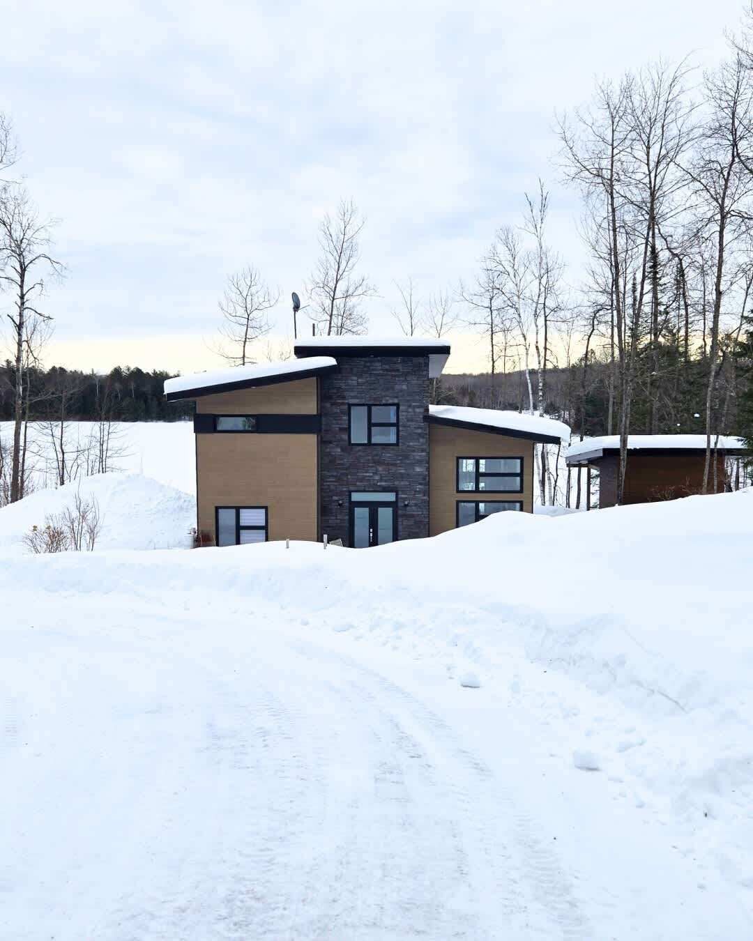Una casa moderna de dos pisos con fachada de piedra, ventanas amplias y un paisaje cubierto de nieve.